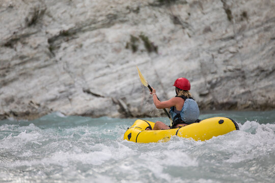 Woman paddles yellow packraft through river rapids