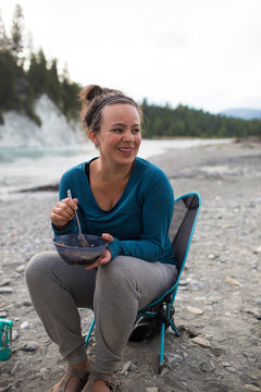 Happy woman eating a meal while camping by a river