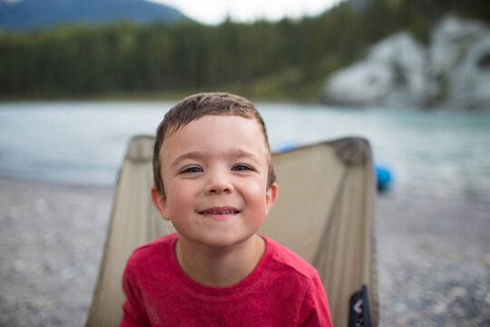 Happy boy sitting in a camp chair by a lake