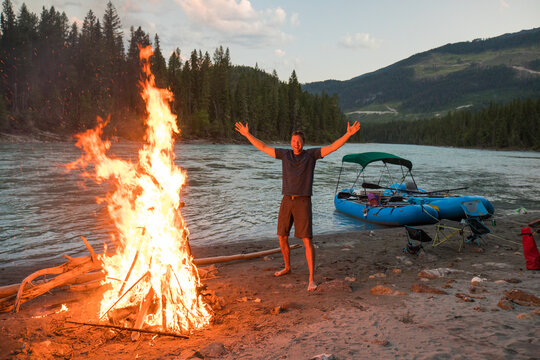 Happy man with arms raised by river campfire