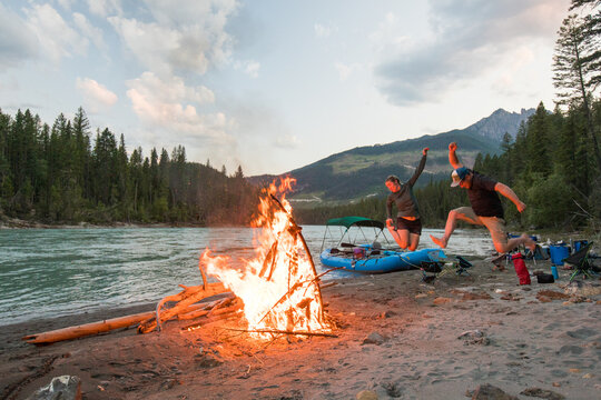 Couple joyfully jumping by a riverside campfire