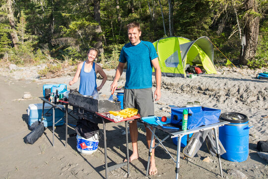 Happy couple cooking breakfast at their beach campsite