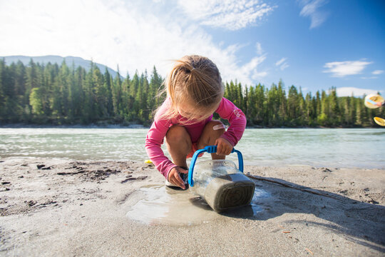 Little girl playing with sand by a river on a sunny day