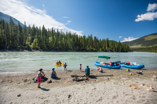 Families enjoying a sunny day on a river bank with rafts