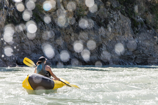 Woman paddles yellow packraft on a sunny river