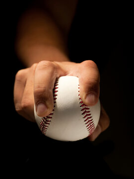 Close up of a hand gripping a baseball against a black background