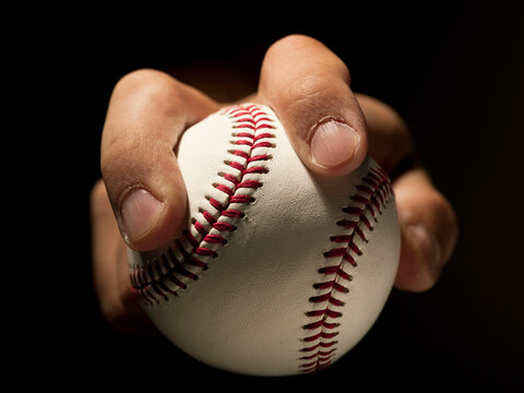 Close up of a hand gripping a baseball against a black background