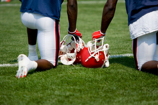 Rear view of two football players kneeling on a green field with