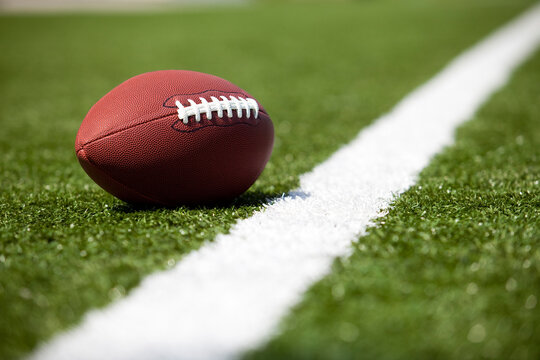 Close up of a football on a green turf field next to a white yard line