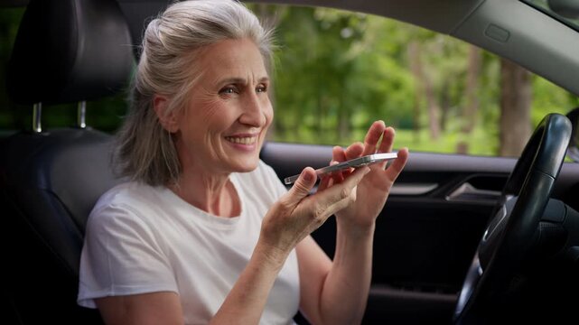 Joyful Caucasian old woman recording audio message smile in automobile sending chatting with vocal command online app phone retired aged female record voice mail talk chat in car auto smiling talking