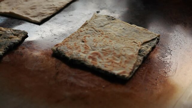 Close-up shot of traditional Turkish stuffed flatbread (gozleme) being flipped and brushed with oil on a hot metal griddle.