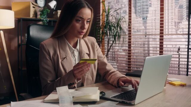 Serious Caucasian business woman paying online with laptop holding credit card businesswoman concentrated girl female executive employer pay shopping with computer online payment taxes bills in office