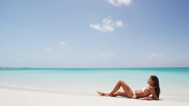 Sexy suntan beach woman sunbathing in fashion bikini. Beautiful fit body of model relaxing tanning on woman. Travel vacation, weight loss or skin care sun protection concept. SLOW MOTION.