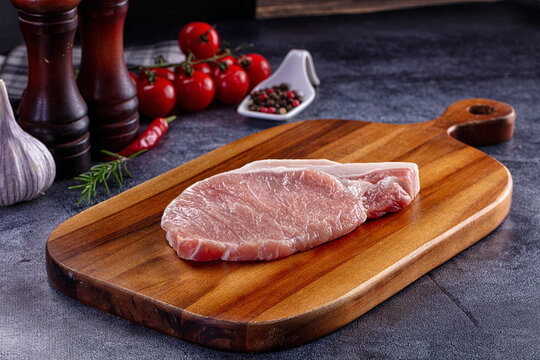 Raw pork steak on wooden cutting board with fresh ingredients