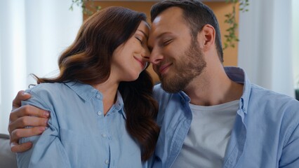 Fototapeta premium Optimistic Caucasian embracing hugging on couch smiling family cuddling embrace at home man with woman date spending time together touch faces cuddle hug anniversary valentine's day tender