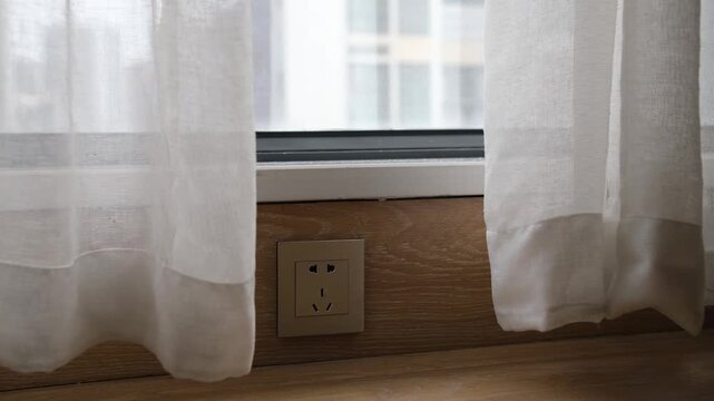 A low-mounted Chinese standard electrical power socket at skirting board level, close to the floor beneath a residential window in a contemporary Chinese apartment interior. Domestic wiring practice
