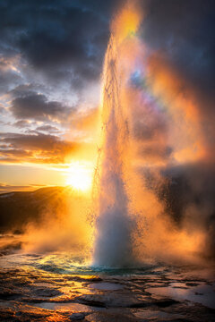 Geyser erupting at sunset in Icelandic geothermal landscape