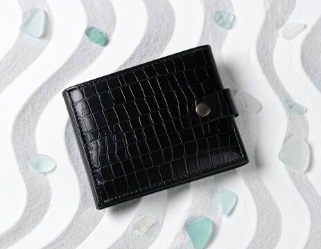 Black stingray leather wallet on white sand mockup for coastal luxury fashion advertising concepts.