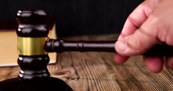 Eye level view of a mahogany judge gavel striking a matching wooden sounding block over a dark rustic wood table background surface