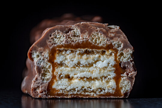 Closeup texture of a cut chocolate candy bar showing wafer layers, flowing caramel and crispy cereal on dark background. Ideal for sweet food advertising, confectionery or menu design