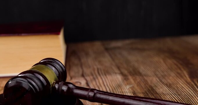 Front angle layout of a mahogany judge gavel striking down on its wooden sound block over a rustic dark desktop background surface