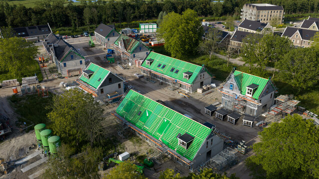 Purmerend, North Holland, Netherlands - 15 June 2026: Aerial view of a residential construction site featuring houses with green roof underlayment, scaffolding, and surrounding trees.