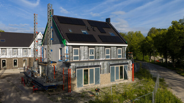 Purmerend, Netherlands - 15 June 2026: Aerial view of a house under construction with black solar panels on the roof and silver insulation foil on the exterior walls.