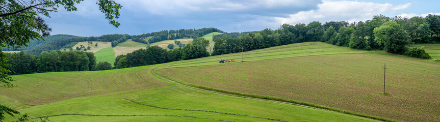 Naklejka premium Rural panoramic view over the Mariazell region in the Vienna Woods near Hafnerberg, Lower Austria, featuring a farmer tilling fields with a tractor in summer