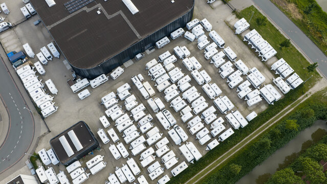 Purmerend, Netherlands - 15 June 2026: Aerial view of a large parking lot filled with numerous white caravans parked in organized rows next to a modern industrial building.