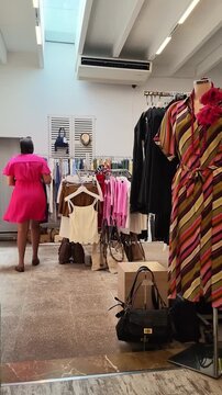 Alcudia Mallorca Spain. 01.06.2026. Video. A woman in a denim dress shops for apparel in a well-lit boutique, surrounded by racks of clothes and accessories