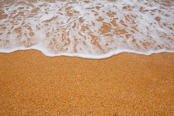 Gentle sea foam washing onto a sandy beach shoreline. Natural coastal background with golden sand and ocean water, perfect for summer, travel and vacation concepts. © Serhii