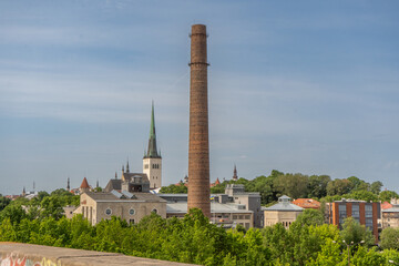 Obraz premium Historic skyline of Tallinn, Estonia, featuring a prominent industrial brick chimney rising above the city's architectural landscape and church spires.