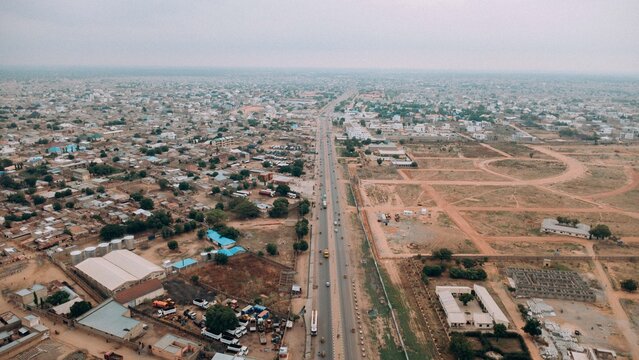 Farawa, Nigeria - 17 June 2026: Aerial view of the urban landscape with a long straight road dividing residential areas and open land under an overcast sky.