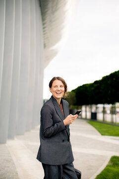Woman using smartphone near modern building during daytime with green space in background