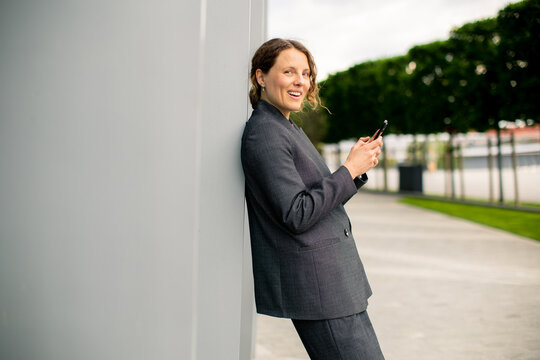 Woman checks phone while leaning against a wall in an outdoor area