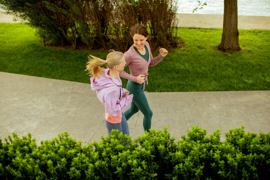 Two women running on a path by the water in a park during the daytime