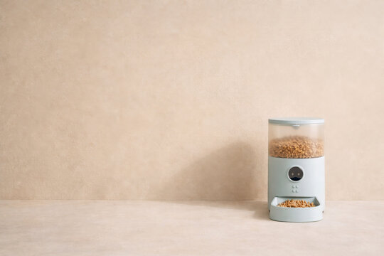 Pet feeder automatic blue dispenser unit filled with dry food kibbles with copy space background