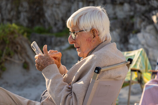 profile of elderly man at beach using mobile phone