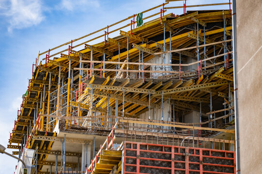 A detailed perspective of a multi story apartment building under construction featuring complex scaffolding falsework and bright yellow structural support formwork beams