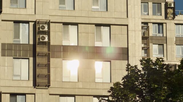 A modern building facade reflects blazing sunlight in Simferopol, Crimea. The dazzling glare creates a warm and vibrant atmosphere near the peaceful green trees.
