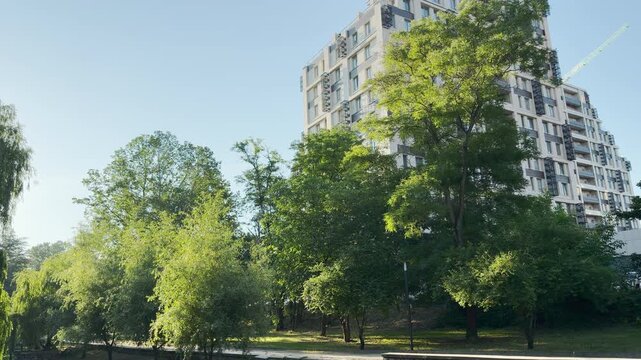 A modern apartment building rises behind a lush green park in Simferopol, Crimea. The sunny day creates a peaceful, cheerful, and fresh feeling.