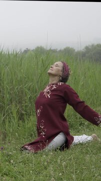 Mature woman doing a pigeon yoga pose in a green field