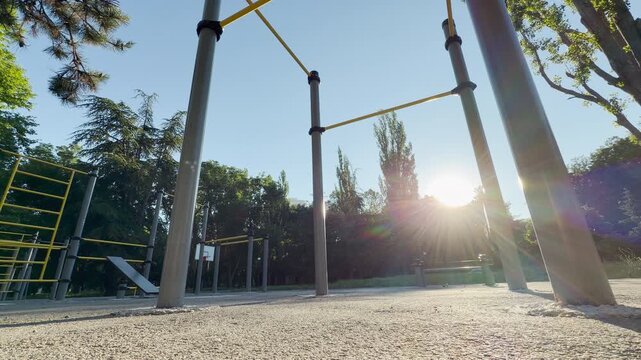 workout bars stand empty under a clear sky. Bright morning sunbeams pierce through lush trees, casting a peaceful, inviting, and highly motivating energy over the park.