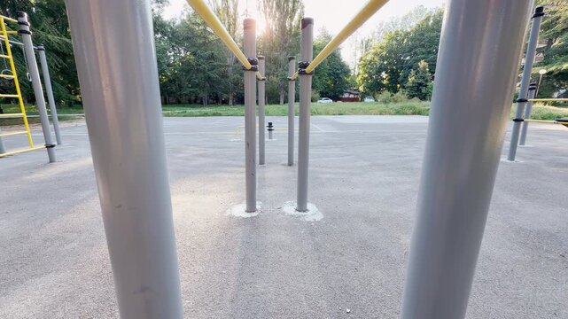 parallel workout bars stand ready for use on an empty outdoor sports ground. The bright morning sun brings a peaceful, motivating feeling to this green park area.