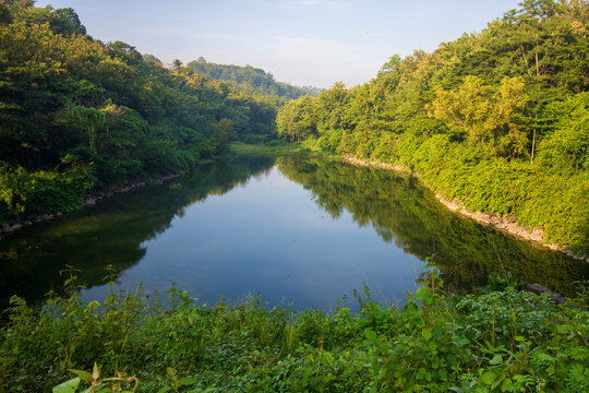 Steep stone staircase structure next to concrete spillway at Sutami dam reservoir surrounded by lush green forest, civil engineering infrastructure in East Java