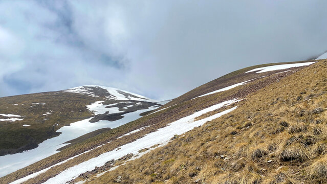 Scenic trekking route near Didi Abuli in Georgia with grassy alpine slopes, melting snow patches and dramatic clouds, wide landscape view, wilderness adventure and outdoor travel.