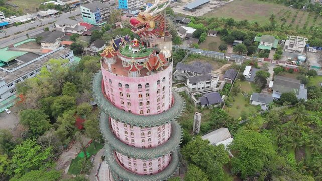 NAKHON PATHOM, THAILAND - MAY 2026: Aerial drone shot pulling back from the giant dragon head to reveal the iconic pink tower temple of Wat Sam Phran.