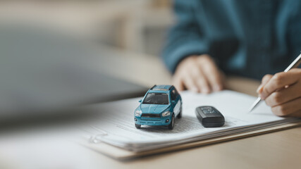 Businessperson signing car purchase agreement with vehicle model and key on contract documents, symbolizing auto financing, ownership transfer, and insurance planning. © Garun Studios