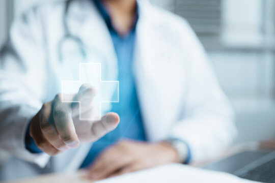 Doctor interacting with an AI-powered healthcare interface displaying a digital medical cross. Ideal for artificial intelligence in healthcare, diagnosis support, patient care.