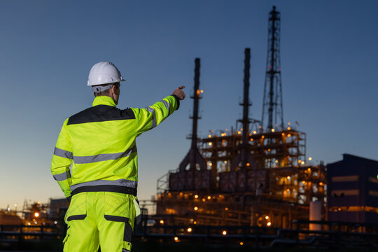 Worker points to oil refinery site at dusk